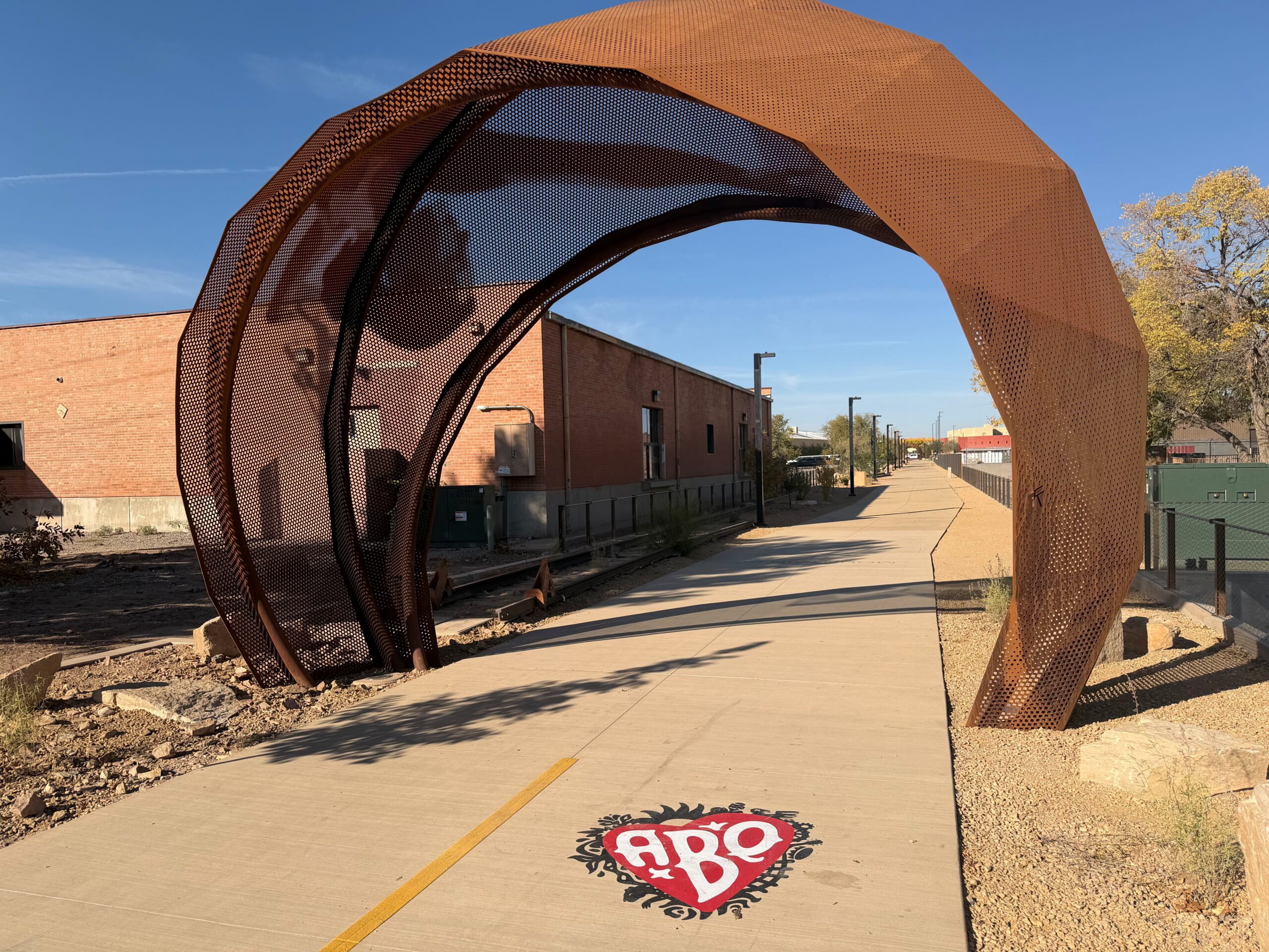 The Flamenco Dancers Gateway Arch at Mountain Road serves as a tribute to the Flamenco Institute, a longstanding cultural institution that has existed in the Sawmill District for decades. The Albuquerque Rail Trail logo is prominently displayed at the entrance, offering a warm welcome to visitors and community residents.